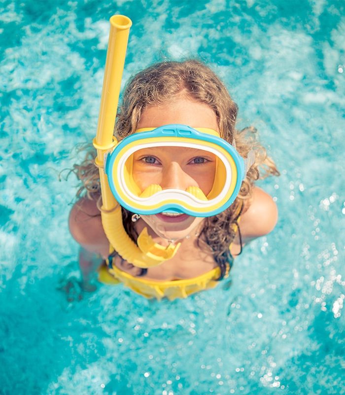 Ein Mädchen was in einem Pool mit Taucherbrille und Schnorchel in die Kamera schaut.
