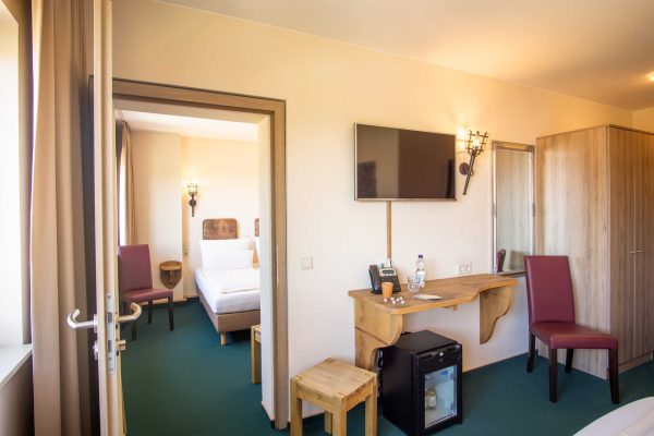 Eine Verbindungstür die zwei normale Doppelzimmer mit einander verknüpft man sieht noch einen Schreibtisch einen Stuhl und eine Minibar auf dem Bild.