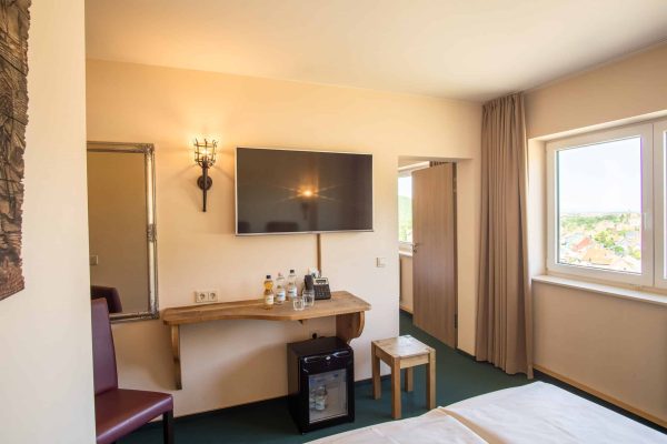 Zweites Doppelzimmer mit Verbindungstür. Aussicht aus der höchsten Etage hin zur Stadt Wernigerode. Flachbildfernseher, Hocker und Schreibtisch sind noch zu sehen.